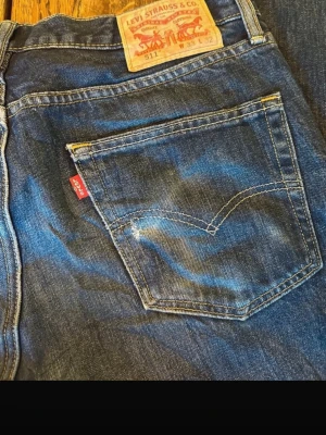 Levi's 511 blå jeans med klassisk look - Säljer ett par blå Levi's 511 jeans med klassisk femficksdesign och den ikoniska röda Levi's-lappen på bakfickan. Jeansen har en rak passform och är tillverkade i slitstarkt denimtyg. Perfekta för dig som gillar tidlös stil och vill ha ett par jeans som funkar till allt.