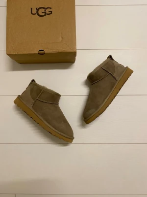 Beige UGG boots i mocka - Säljer ett par klassiska beige boots från UGG i mjuk mocka med foder på insidan. Skorna har en låg siluett, rund tå och platt sula i gummi. Perfekta för kalla dagar och riktigt sköna att ha på sig. Nya i storlek 38 men känns lite mindre så passar även 37/37.5