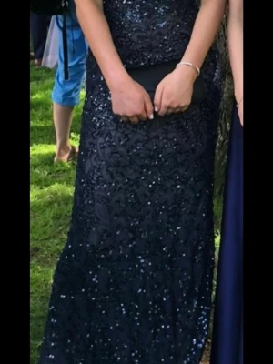 Mörkblå balklänning - Säljer en superfin  mörkblå balklänningen  med glittriga paljetter och vackert mönster. Klänningen har öppen rygg och figurnära passform. Strl 36 men passar även 38. Är 170 cm. Köpt för 4000kr från dressroom