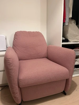 Rosa recliner fåtölj i tyg - Mysig rosa recliner fåtölj med bred sits och tjocka armstöd. Klädseln är i mjukt tyg och fåtöljen har ett utfällbart fotstöd som gör det enkelt att luta sig tillbaka. Perfekt för att chilla i sovrummet eller vardagsrummet. Modern design med rundade former.