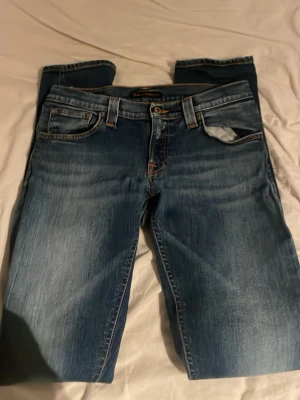 nudie w29 L32 slim fit - Snygga blå jeans från Nudie Jeans med klassisk femficksmodell och kontrastsömmar på bakfickorna. Jeansen har normal passform och är tillverkade i slitstarkt bomullsmaterial. Perfekta för en avslappnad och stilren look.