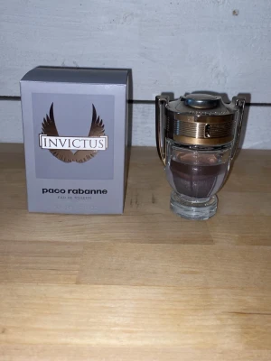 Paco Rabanne Invictus Eau de Toilette - Paco Rabanne Invictus Eau de Toilette med en unik troféformad flaska i glas och silverfärgad metall. Doften kommer i en stilren grå förpackning med bronsdetaljer och logga. Perfekt för dig som gillar fräscha och maskulina parfymer.