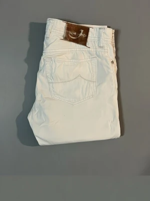 Vita jeans från Jacob Cohen - Snygga vita jeans från Jacob Cohen i storleken 32. Jeansen har en broderad med style 688 på insidan och en fet patch i brunt med det unika hästmaterialet Perfekta för dig som vill ha en clean och stilren look inför sommaren 
