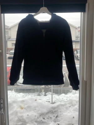 Svart bomberjacka med grått foder - Snygg svart bomberjacka med mjukt grått teddyfoder på insidan. Klassisk passform med ribbade muddar vid ärmar och midja samt dragkedja framtill. Perfekt för dig som vill ha en stilren och bekväm jacka med extra värme.