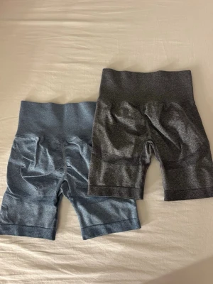 Två par höga cykelshorts - Säljer två par höga cykelshorts i sömlös design, ett par i mörkgrått och ett par i blått. Perfekta för träning eller chill, med bred resår i midjan för extra komfort. Materialet är stretchigt och känns mjukt mot huden.
