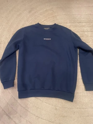 Blå sweatshirt från McKenzie - Mörkblå sweatshirt från McKenzie med rund halsringning och diskret logga på bröstet. Tröjan har långa ärmar, ribbade muddar och är gjord i mjukt material som passar perfekt till en avslappnad stil.