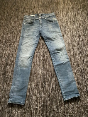 Replay Anbass blå jeans slim fit - Säljer ett par Replay Anbass jeans i ljusblå tvätt med slim fit. Klassisk femficksmodell med snygga slitningar och vita sömmar. Perfekta för dig som gillar en smalare passform och stilren look.Var inte rädd för att skicka om du har någon fråga eller vill ha fler bilder!