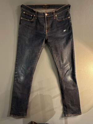 Mörkblå Nudie Jeans med Slitningar  -  Mörkblåa Nudie jeans med slitningar||Skick 8/10||Storlek W31/L34||Modellen på bilden är 184 och väger ungefär 65kg||Skriv vid minsta intresse||