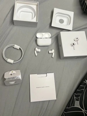 Apple AirPods Pro med laddningsetui - Säljer ett par vita Apple AirPods Pro med trådlöst laddningsetui. Hörlurarna har en stilren och kompakt design, levereras med originalförpackning, laddkabel och extra öronproppar. Perfekta för musik, samtal och träning tack vare brusreducering och smidig passform.