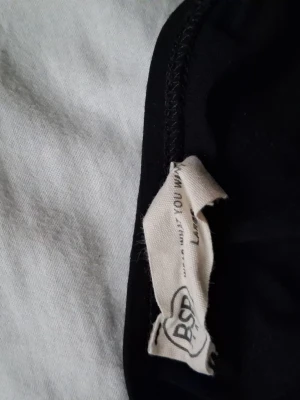 Svart croppad topp från BST - Snygg svart croppad topp från BST med breda axelband och en enkel design. Perfekt att matcha med jeans eller kjol för en cool och avslappnad look. Materialet känns mjukt och stretchigt, vilket gör den bekväm att bära hela dagen.