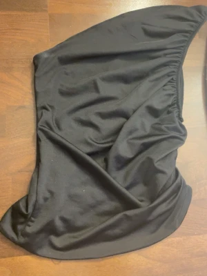 Svart one shoulder topp från H&M - Snygg svart one shoulder topp från H&M i stretchigt material. Toppen har en asymmetrisk design med resår upptill för att sitta på plats. Perfekt att styla med höga jeans eller kjol för en trendig look.