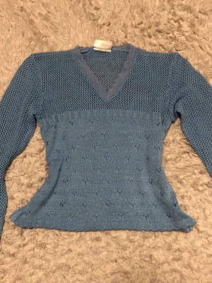 Blå stickad tröja Side by Side - Snygg blå stickad tröja från Side by Side med V-ringning och lång ärm. Tröjan har två olika stickmönster, ett tätare nertill och ett mer öppet upptill samt runt halsen. Perfekt för dig som gillar unika detaljer och mjuka material.