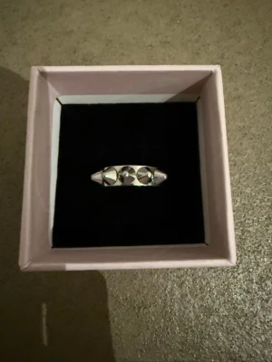 Silvrig ring med nitar - Säljer en cool silvrig ring med tre runda nitar på ovansidan. Ringen har en modern och edgy design som sticker ut och passar perfekt för dig som gillar detaljer med attityd. Materialet är metall i blank finish och ringen levereras i en snygg ask.