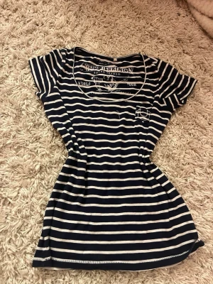 Randig marinblå t-shirt med tryck - Snygg marinblå och vitrandig t-shirt från True Religion med korta ärmar och rund hals. T-shirten har coola tryckdetaljer både fram och bak samt en liten broderad figur längst ner. Perfekt för dig som gillar casual och marint inspirerad stil. Storleken är S och passar jättebra! Dessutom är den super bekväm och fin!