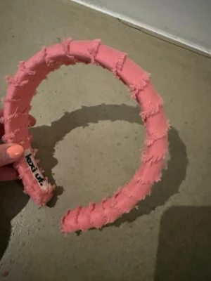 Rosa diadem från Lexuf - Säljer ett rosa diadem från Lexuf med fransig textil och trendig, chunky design. Diademet har en bred form och är täckt av tyg med råa kanter för en cool och avslappnad look. Perfekt accessoar för att lyfta din outfit.