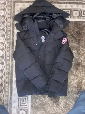Canada Goose Jacket Black Wyndham XS - Slidern på dragkedjan är upp och ner vilket gör så att man dragkedjan inte funkar MEN 1. Det finns knappar på jackan att använda medans som funkar precis lika bra och 2. Det går såklart att laga. 100% water-resistant super varm jacka