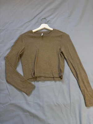 Grön  ribbad croppad långärmad topp - Trendig grön croppad topp med lång ärm och ribbad struktur. Perfekt till höga jeans eller kjol. Enkel och stilren design som passar till många olika looks.