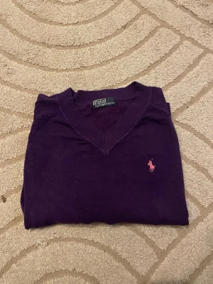 Ralph Lauren 100% Cashmere❤️ - Lila stickad tröja från Polo Ralph Lauren 100% Cashmere med V-ringning och lång ärm. Tröjan har en rosa broderad logga på bröstet och ribbstickade muddar vid ärmslut och nederkant. Perfekt för lager-på-lager och snygg till jeans. Använd gärna köp nu❤️