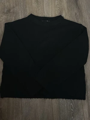 Svart stickad tröja  - En enkel och stilren svart stickad tröja med rund hals och långa ärmar. Tröjan har en rak passform och är tillverkad i ett mjukt stickat material. 
