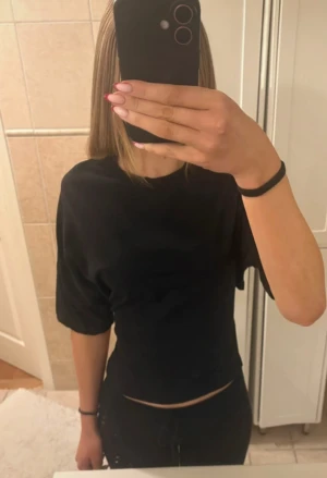 Svart topp med öppen rygg och knyt - Säljer en svart topp med korta ärmar och croppad passform. Toppen har en snygg öppen rygg med knytband som ger en unik look. Perfekt till jeans eller kjol för en trendig outfit🥰