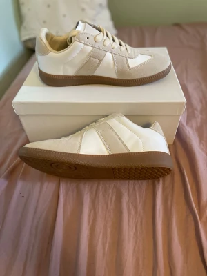 Maison margiela gats - Stilrena Maison margielas i vitt läder med beige mockadetaljer och klassisk gummisula. Snygg retrodesign med lågt skaft och vita snören. Perfekta för dig som gillar minimalistisk och tidlös stil. Skorn är helt oanvända men boxen har lite småskråmor. Priset är ej hugget i Sten så hör gärna av er vid prisförslag eller funderingar😊