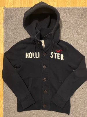 Vintage Hollister Cardigan Med Knappar - Väldigt sällsynt och vintage Hollister hoodie med knappar | Tröjan är i väldigt bra skick utan defekter! | Längd ≈ 63cm, Bredd armhåla-amrhåla ≈ 53cm | Modell 175cm, 68kg | Hör av vid ytterligare frågor och priset kan diskuteras vid snabbt köp! |