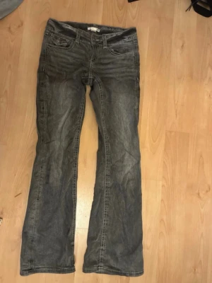 Grå bootcut jeans med fickdetaljer - Ett par lowwaist grå bootcut jeans med fickor där bak. De har en lätt tvättad look. Det enda som man behöver göra med jeansen är att stryka de så blir de som nya! De är i storlek 152 och är från Gina Young.