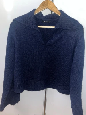 Mörkblå stickad tröja Gina Tricot - Mörkblå stickad tröja från Gina Tricot med krage och v-ringning. Tröjan har långa ärmar och är breda, ribbade längst ner vid ärmslutet och nederkant med slits. 