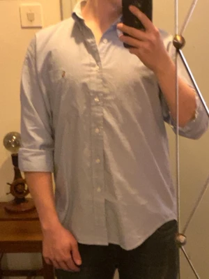 Ralph Lauren skjorta M men sitter som L - Skjortan är  i en fin ljusblå färg som passar perfekt under tjocktröjor eller som huvudplagg mot våren och sommaren. Tröjan är relativt lång och stor för att vara i m så ha det i åtanke