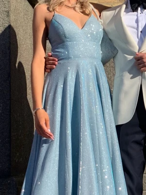 Ljusblå glittrig långklänning - Säljer en ljusblå långklänning med glittereffekt och smala axelband. Klänningen har v-ringad urringning och ett svepande, utsvängt kjolparti. Perfekt för bal eller student! Klänningen är uppsydd av skräddare, jag är 170 cm lång och var även klackar. Klänningen är en aning smutsig vid kanten men är inte super synligt (skriv för bild). Köpt på Dressroom linne i Göteborg, orginalpris 4500. Står storlek 2 men skulle säga att den passar en xs/s i storlek