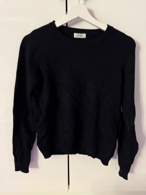 Svart stickad tröja Jacqueline de Yong - En enkel och stilren svart stickad tröja från Jacqueline de Yong. Tröjan har rund halsringning, långa ärmar och ribbade muddar vid ärmslut och nederkant. Perfekt basplagg till garderoben och lätt att matcha med olika outfits.