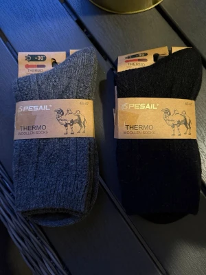 Pesail Thermo ullstrumpor 43-47 - Två par varma Thermo ullstrumpor från Pesail i storlek 43-47. Ena paret är mörkgrå och det andra är svarta. Perfekta för kalla dagar med sin tjocka, ribbade ullkvalitet som håller fötterna varma även vid riktigt låga temperaturer. Vädras i första hand. 