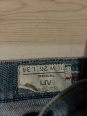 Blå Diesel LIV jeans W26 L34 - Säljer ett par klassiska blå jeans från Diesel, modell LIV. Jeansen har raka ben, fem fickor och stretchigt material för extra komfort. Perfekta för en avslappnad och trendig look. Passar dig som gillar tidlös denimstil.