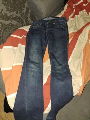 True Religion bootcut jeans blå - Säljer ett par blå bootcut jeans från True Religion med snygga kontrastsömmar och ikoniska bakfickor med lock och knapp. Klassisk femficksmodell i denim med låg midja. Joey low rise i storlek 23. I okej skick men nötta nere vid hälen. 