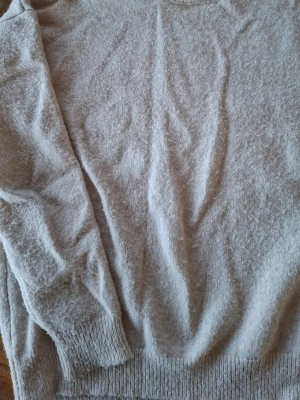 Beige stickad tröja med rund hals - Mysig beige stickad tröja med rund hals och långa ärmar. Tröjan har ribbstickade muddar vid ärmslut och nederkant. Perfekt för lager-på-lager och enkel att matcha med olika outfits.