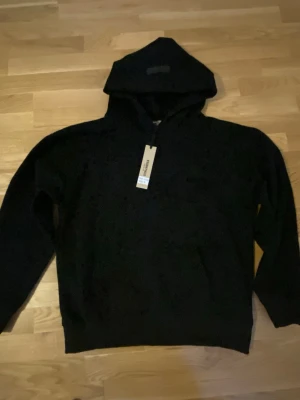 Svart hoodie essential - Säljer en stilren svart hoodie med klassisk huva och magficka. Hoodien har ribbade muddar vid ärmslut och nederkant samt en diskret dragkedja vid halsen. Perfekt för dig som gillar en enkel och clean look.