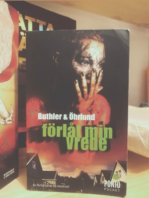 Förlåt min vrede 🩸 - En spännande pocketbok med titeln 'Förlåt min vrede' av Buthler & Öhrlund. Omslaget har mörka och röda toner med en dramatisk bild och grönt texttryck. Perfekt för dig som gillar kriminalromaner och spänning.