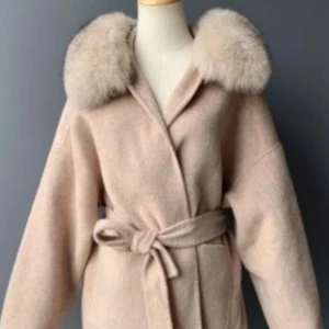 Beige kappa med päls  - Bilderna i annonsen är från hemsidan, men självklart kan jag skicka bilder på kappan vid intresse skriv bara. Kappan är i jättebra skick använd 2 gånger sens jag köpte den, men dock inga tecken på att den används. Passar både hösten och våren. Pris kan diskuteras 