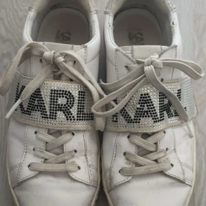 Vita sneakers från Karl Lagerfeld - Snygga vita sneakers från Karl Lagerfeld med glittriga detaljer och stora strassprydda band över vristen där det står KARL. Skorna har snörning, rund tå och präglad logga på sulan. Perfekta för dig som vill sticka ut med lite extra bling. Skorna är väl använda men ändå omhändertagna. Går absolut att fräscha upp dem så de blir nästan som nya igen! 🥰NYPRIS: 1 500:- (jag kan även tvätta dem innan jag postar dem)