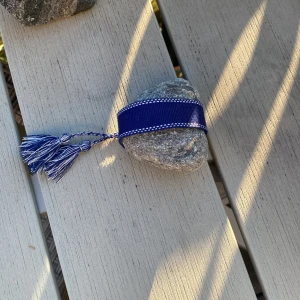 Blått bälte med tofsar - Snyggt blått bälte med vita detaljer längs kanterna och två dekorativa tofsar i änden. Bältet är brett och har en mjuk känsla, perfekt för att ge outfiten en cool touch. Passar dig som gillar att sticka ut med accessoarer.