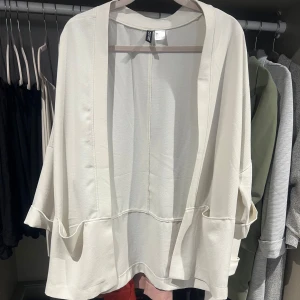 Vit bluskavaj - Säljer min bluskavaj med lös passform och stora fickor framtill. Den har trekvartsärmar med uppvik och är tillverkad i ett mjukt, lätt material som passar perfekt till vår och sommar. Enkel att slänga på över en topp för en chill look.