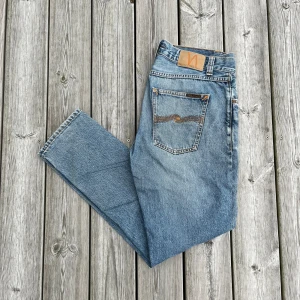 Nudie Jeans blå straight fit W31 L30 - Säljer ett par klassiska blå jeans från Nudie Jeans i rak modell. Jeansen är i bra skick förutom att dom är lite smutsiga längst ner vi fötterna (se bild). Annars är de fräscha och snygga. Säljer för att de är för stora för mig i midjan.