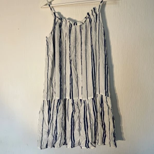 Vit och marinblå randig sommarklänning H&M - Säljer en luftig vit klänning med marinblå ränder från H&M. Modellen är kort med smala axelband och har en volang nedtill. I storlek 34. Ny med prislapp