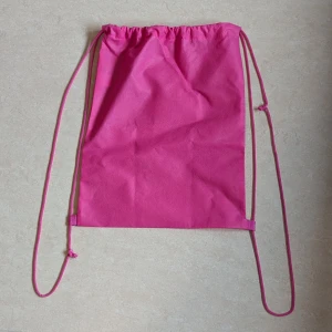 Rosa påse med snörning - Enkel och smidig rosa påse med snörning som axelband. Tillverkad i lätt syntetmaterial och har en stilren, enfärgad design.