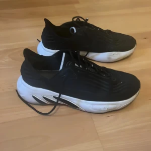 Svarta Adidas sneakers strl 47⅓ - Säljer ett par svarta Adidas sneakers med vit sula och snygga vågformade detaljer. Skorna har snörning och en sportig vibe, perfekta för dig som gillar streetstyle. Adidas-logga på plösen och bekväm passform. Riktigt schyssta till både jeans och shorts.