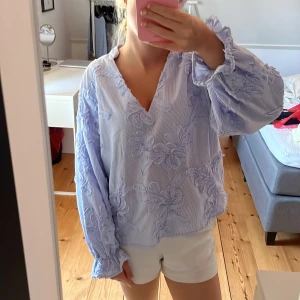 Blå blommig blus från Zara XS - Superfin blus från Zara i ljusblått med tunna vita ränder och broderade blommor. V-ringad med långa puffiga ärmar och resår vid ärmslut. Den är i storlek xs och är i nyskick, använd 1 gång❣️Nypris 399❣️