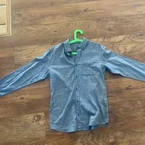 Blå långärmad skjorta i bomull - Snygg blå skjorta från Essental i mjuk bomull. Klassisk modell med knappar framtill och bröstficka. Aldrig använd/som ny 