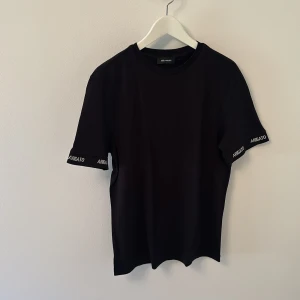 Axel Arigato  - Svart t-shirt från Axel Arigato med logga broderad i vitt på ärmarna. Klassisk rund halsringning och rak passform. Perfekt för en clean och stilren look.