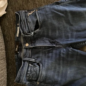 Replay Anbass slim fit jeans blå - Snygga blå Replay Anbass jeans i slim fit med klassisk femficksdesign och snygga detaljer på bakfickorna. Jeansen har en mörk tvätt och är tillverkade i mjukt jeansmaterial som sitter skönt hela dagen. Liten i storleken passar 32 i midjan