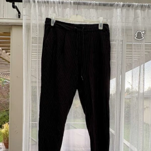 Svarta randiga byxor från Noisy May - Säljer ett par svarta byxor från Noisy May med tunna vita ränder. Byxorna har dragsko i midjan och är i en mjuk och bekväm bomullsblandning. Perfekta för en chill och stilren look.